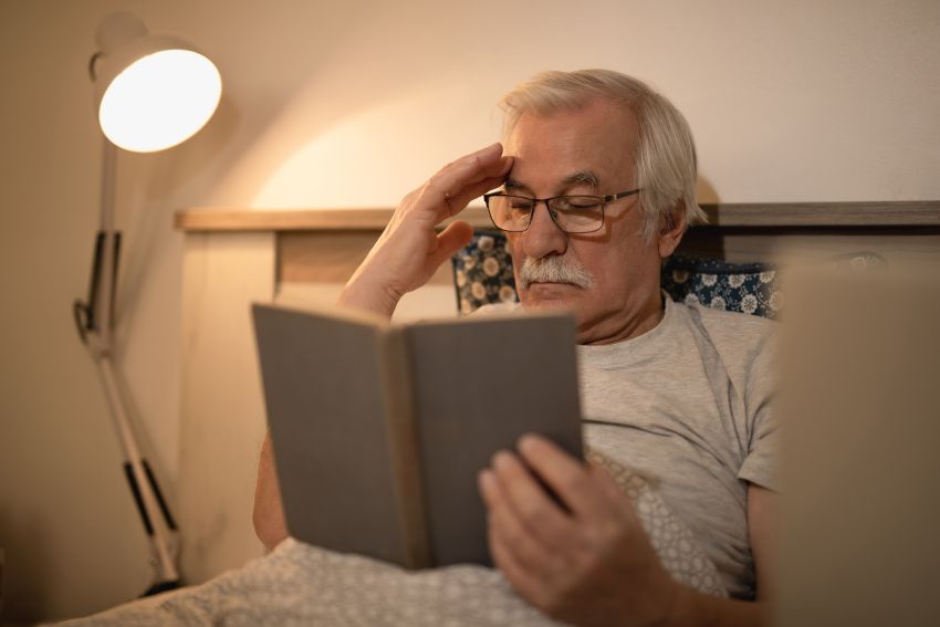 senior man reading book lying on bed 